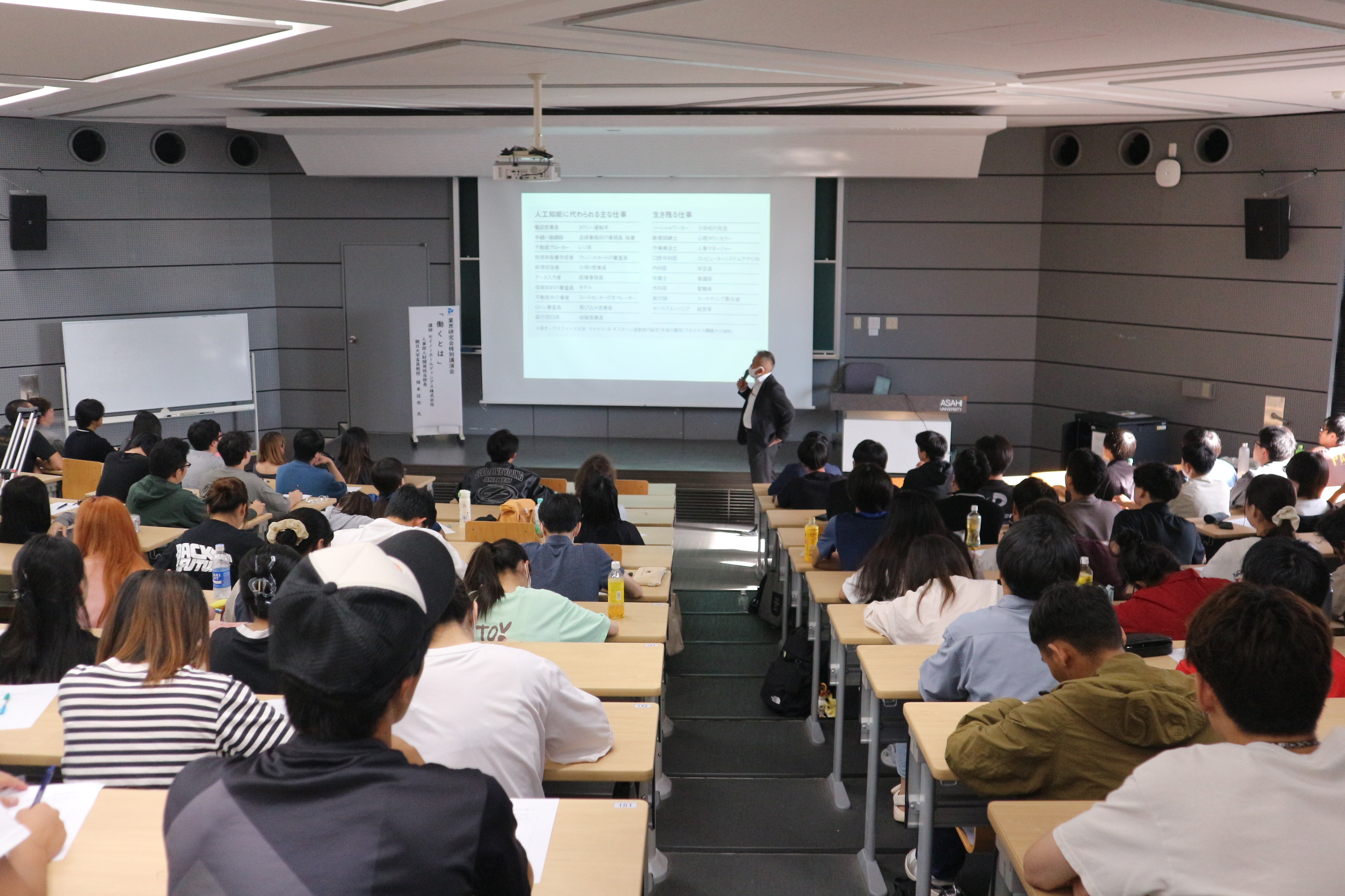 100名を超える学生がメモをとりながら講義を聞く様子